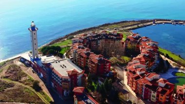 Turuncu duvarları ve kırmızı çatıları olan, yarımadadaki uzun bir deniz fenerinin yanındaki dairesel yerleşim alanının yüksek açılı drone görüntüsü. Bulgaristan.