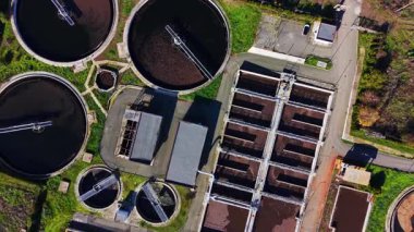 Endüstriyel su arıtma tesisinde yeşil çimenli büyük dairesel ve dikdörtgen filtreleme tanklarının doğrudan yukarıdan görüntüsü..