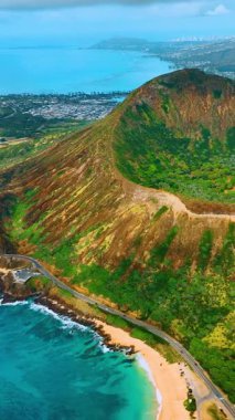 Geniş bir kumsal manzarası, turkuaz su, kıyı yolu ve mavi bir gökyüzünün altındaki volkanik kraterin yamaçları. Sandy Beach Park ve Koko Head 'in hava manzarası. Dikey video.