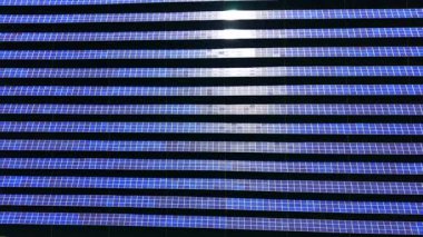 Mavi panelleri ve parlak güneş ışığı yansıması olan bir fotovoltaik güneş enerjisi santralinin yukarıdan aşağı perspektifi. Güneş panelleri parlak güneş ışığını yansıtan sıralar.