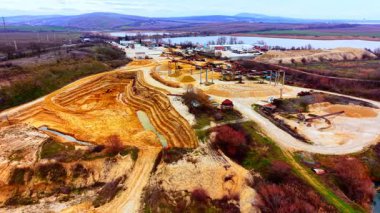 Açık çukur kazma alanı, teraslı duvarlar, makineler ve bulutlu gökyüzü altında su birikintileri. Endüstriyel kum ocağı ve işleme alanının hava manzarası.