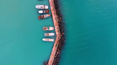 Birkaç küçük tekne, turkuaz ve derin mavi sularda beton bir dalgakıran boyunca kenetlendi. İskeleye demirlemiş balıkçı teknelerinin üst hava manzarası.