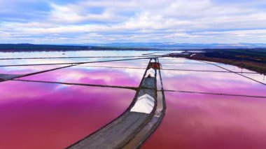 Pembe tuz buharlaşma göletleri arasındaki uzun yollarda bulutlu bir gökyüzünün altında toplanmış büyük beyaz deniz tuzu yığınları bulunur. Bulgaristan 'ın hava manzarası.