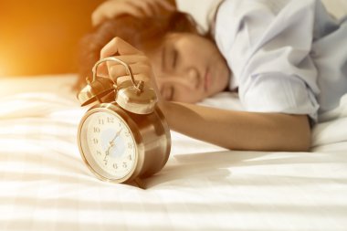 Genç Asyalı kadın yatakta çalar saat ile uyanmak çalışıyor
