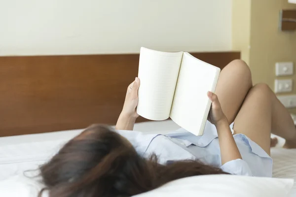 Молода жінка читає книгу, лежачи на ліжку — стокове фото