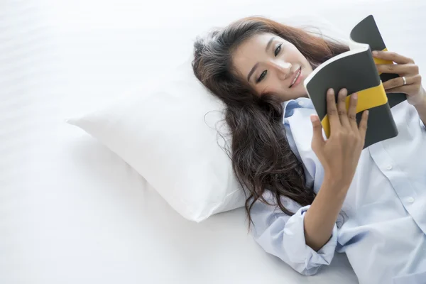 Nuori nainen lukee kirjaa makatessaan sängyllä — kuvapankkivalokuva