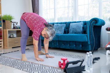 Mature woman doing exercise to stretch legs muscle with Bends down and touches the floor  with two hands and Both legs are straight. Home workout concept