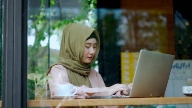 Temiz camdan, portreden, dizüstü bilgisayarda yazan ve ekrana bakan güzel Müslüman kadının kahve dükkanında mutlulukla çalışırken, Müslümanların iş konseptinden.