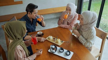 Genç Müslüman adam ve üç güzel kadın kafeteryada dinleniyorlar, birlikte pastane, pasta ve meşrubat yemekten zevk alıyorlar.