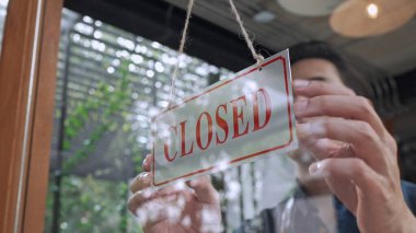 Pencereden bak, yakışıklı genç sahibinin kafeye veya restorana kapanmak için vitrin levhası asmasını çek, küçük işletme hizmeti kavramı.
