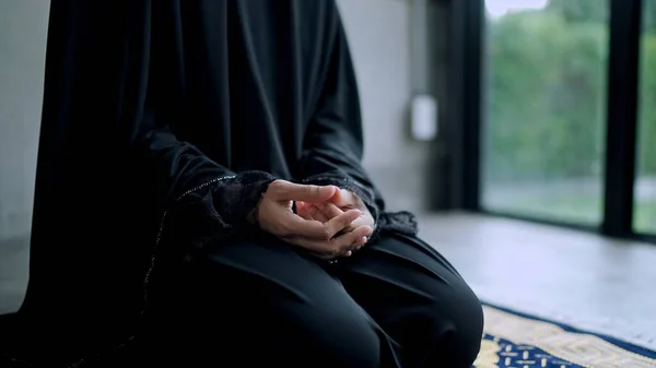 若いです美しいですイスラム教徒女性身に着けています黒ヒジャーブ座っていますマットの上に彼女の祈りと家で経典を読む — ストック写真