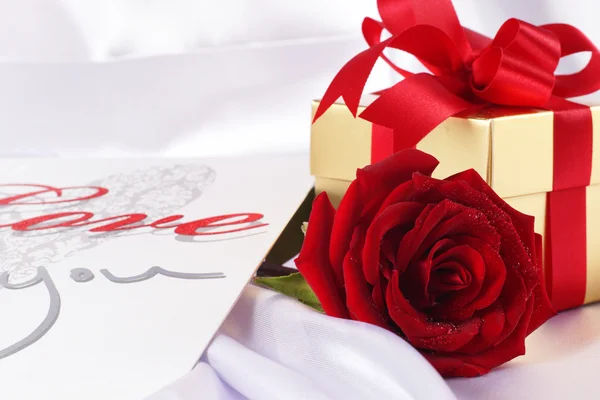 Golden gift box and red roses on white satin background — Stock Photo, Image