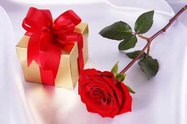 Golden gift box and red roses on white satin background — Stock Photo, Image