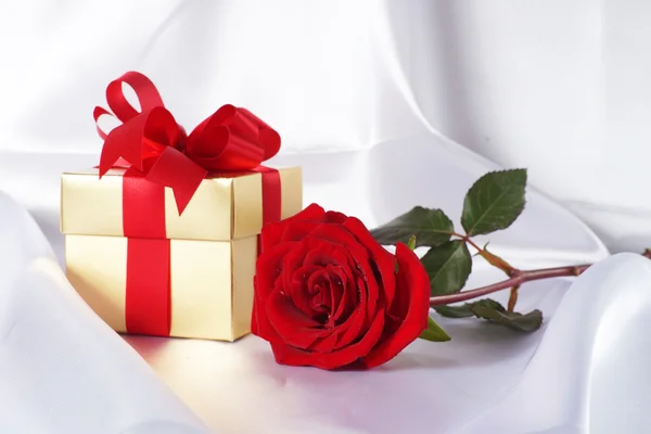 Golden gift box and red roses on white satin background Royalty Free Stock Photos