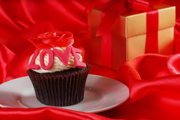 Cupcake with a red rose on top and gifts in boxes on red satin b — Stock Photo, Image