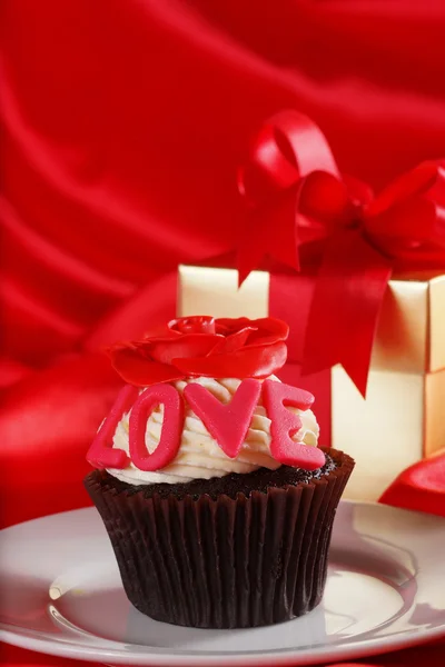 Cupcake with a red rose on top and gifts in boxes on red satin b — Stock Photo, Image