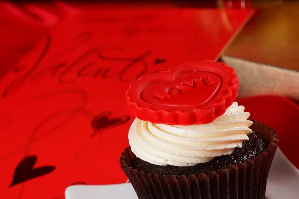 Cupcake com um coração vermelho no topo e presentes em caixas de cetim vermelho — Fotografia de Stock