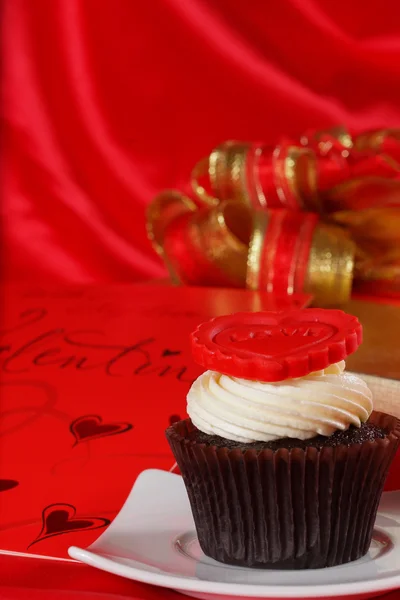 Cupcake com um coração vermelho no topo e presentes em caixas de cetim vermelho — Fotografia de Stock