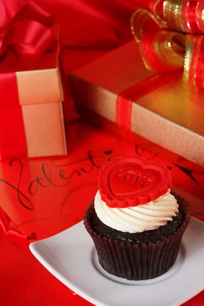 Cupcake with a red heart on top and gifts in boxes on red satin — Stock Photo, Image