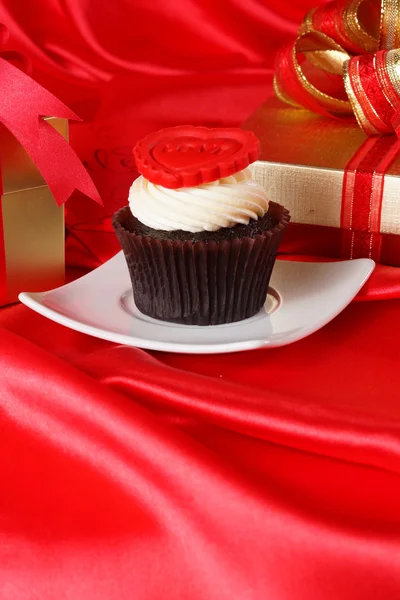 Cupcake con un corazón rojo en la parte superior y regalos en cajas en satén rojo — Foto de Stock