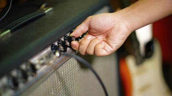 Hand turn knob of guitar amplifier with Electric Guitar on the background, shallow depth focus.