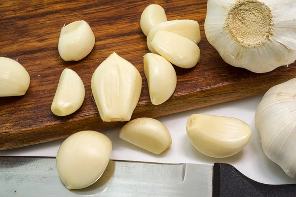 Bulbos y clavos de ajo blanco, pelados sobre tabla de cortar de madera — Foto de Stock