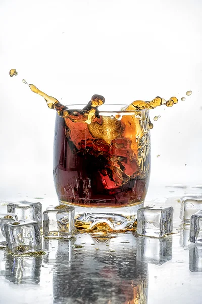 Cubo di ghiaccio caduto nel bicchiere di cola e spruzzi di cola — Foto Stock