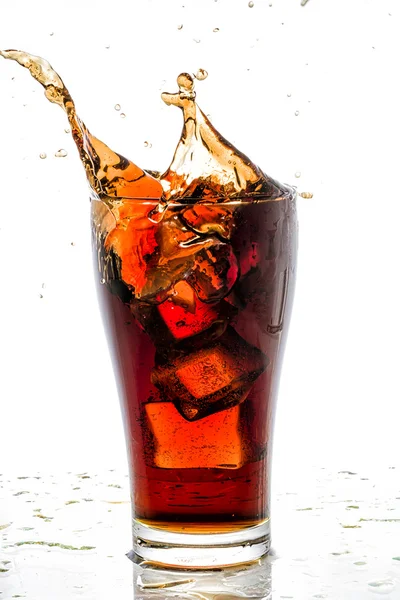 Cubo di ghiaccio caduto nel bicchiere di cola e spruzzi di cola — Foto Stock