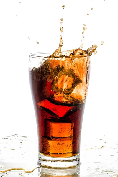 Cubo di ghiaccio caduto nel bicchiere di cola e spruzzi di cola — Foto Stock