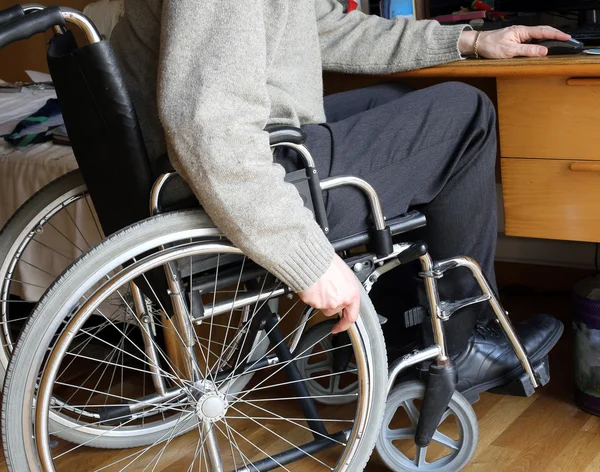 Person sitting in a wheelchair at a desk with pc — Stock Photo, Image