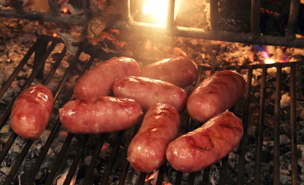 Pork sausages on the grill of the fireplace with fire burning Royalty Free Stock Images
