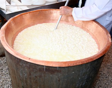cheesemaker curds che yapmak için bakır kazana kıpırdanırken.