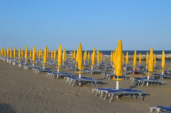 Gelbe geschlossene Sonnenschirme am Strand mit Liegestühlen — Stockfoto