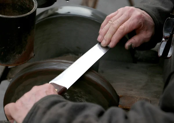 Grinder with large hands sharpen a knife — Stock Photo, Image