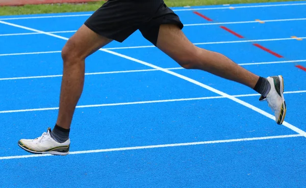 Gambe di corridore veloce corre in blu nella pista di atletica — Foto Stock