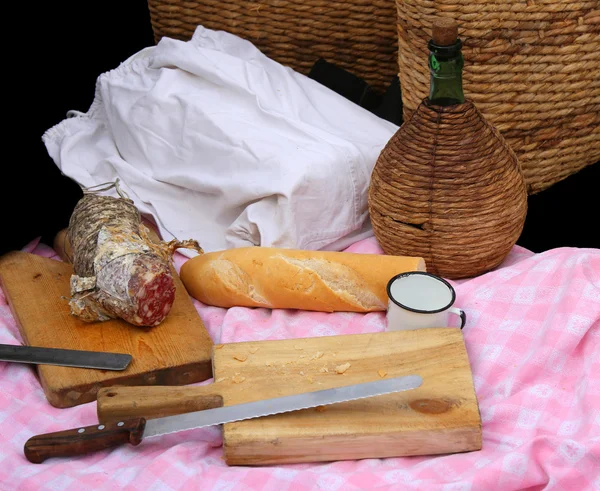 Picinc com salame, pão e faca e frasco de vinho — Fotografia de Stock
