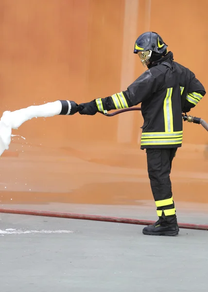 Bombeiro com um extintor com espuma sob o fumo laranja — Fotografia de Stock