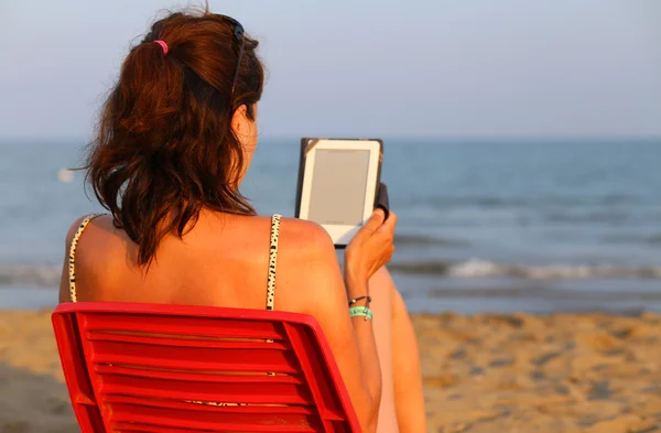 Kobieta na czerwone krzesło odczytuje ebook na plaży — Zdjęcie stockowe