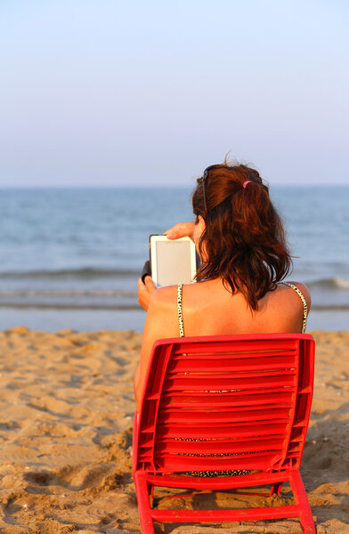 woman reads the ebook on the beach by the sea in summer
