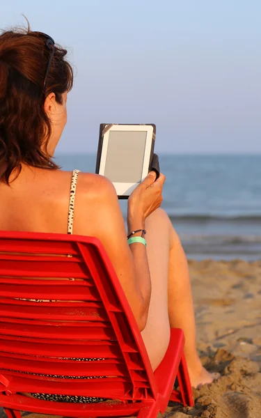 Beautiful woman reads the ebook on the beach — Stock Photo, Image