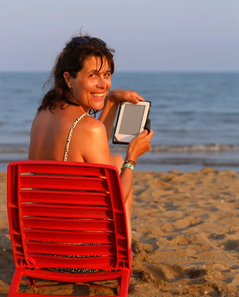 Donna legge l'ebook sulla spiaggia in riva al mare in estate — Foto Stock