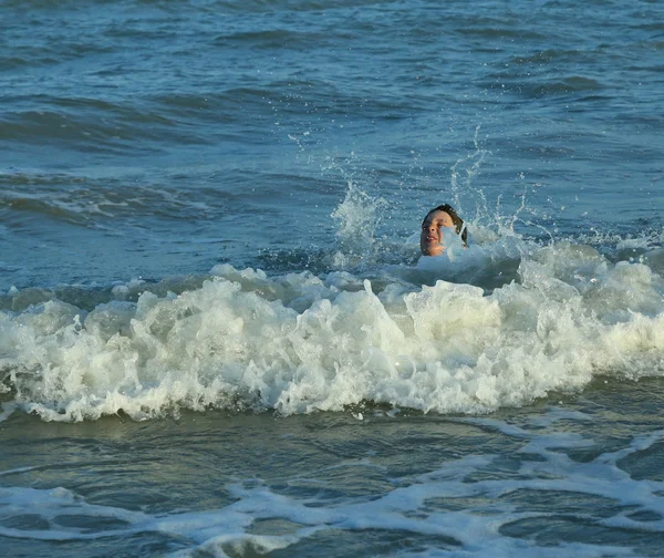 Мальчик играет, прыгая по морским волнам летом — стоковое фото