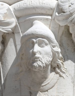 Beyaz yüzlü, sakallı, uzun saçlı, tarihi binanın taşına kazınmış bir adam.