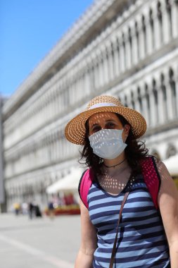 Saint Mark Meydanı 'ndaki tecrit sırasında İtalya' da Venedik 'i ziyaret ederken maske ve hasır şapkalı hoş bir genç kadın.