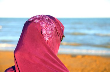 Kocasının deniz kenarına gelmesini beklerken Arap peçeli genç bir kadın.