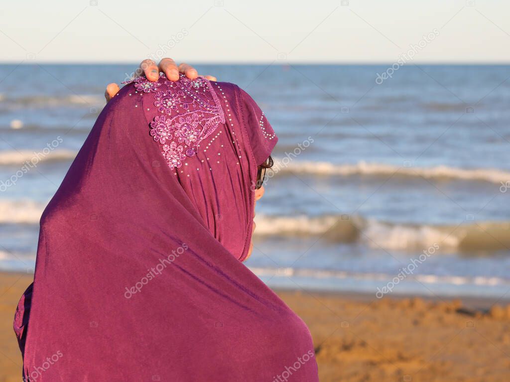 young girl with hand on veil on head by the sea in summer at sunset