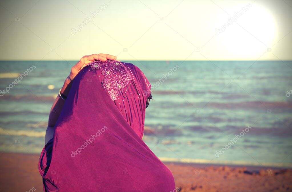 young girl with hand on veil on head by the sea in summer with special toned effect and the sun