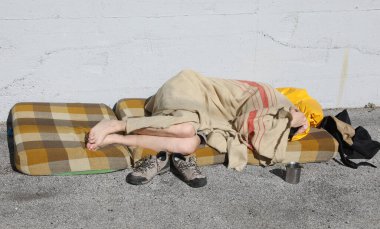 Çıplak ayaklı evsiz. Şehir sokaklarında pis bir yatakta uyuyor.