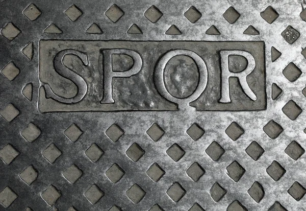 Metal rögar kapağındaki SPQR metni İtalya 'daki Roma şehrinin kısaltmasıdır ve İtalyan dilinde Roma Senatosu ve Halk anlamına gelir.