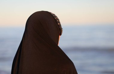 Yazın deniz kenarında siyah elbiseli Arap kadın saçlarını kapatıyor.